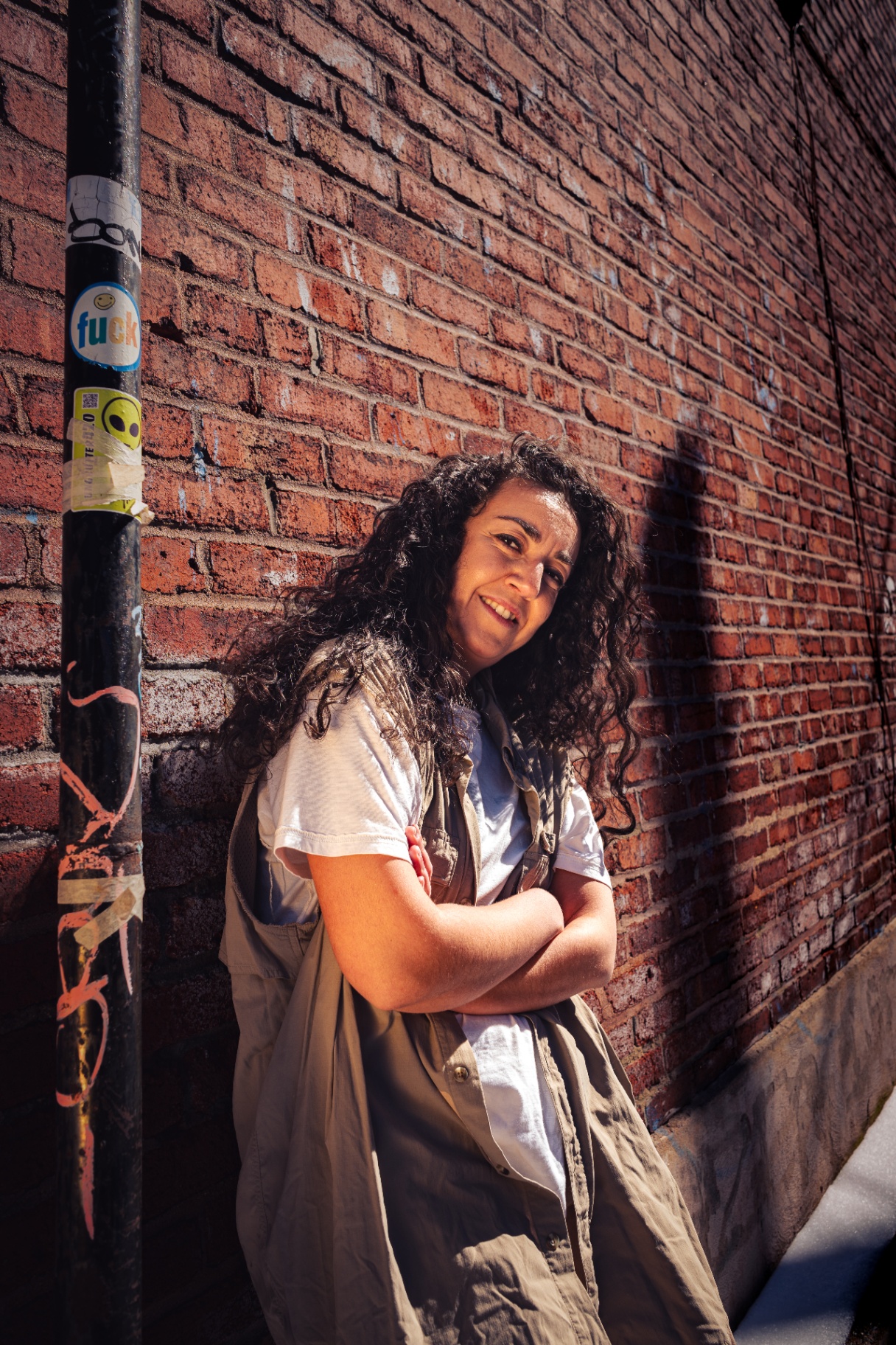 Smiling community member leaning against a sunlit Montreal brick wall.